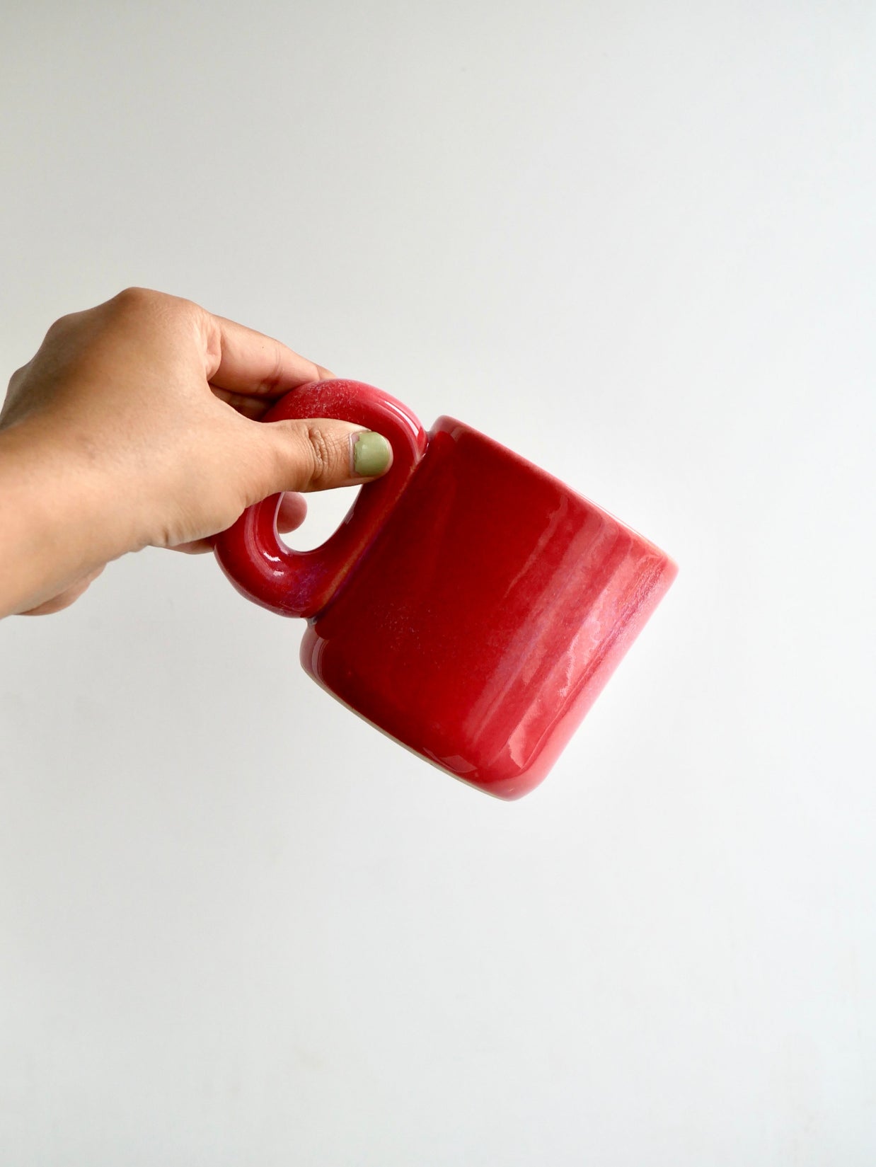 Hand holding a ceramic red glossy mug against a white background