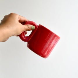 Hand holding a ceramic red glossy mug against a white background
