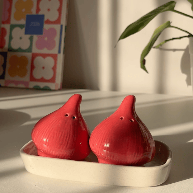 A pair of red onion shaped salt and pepper shakers set with a white ceramic tray. 