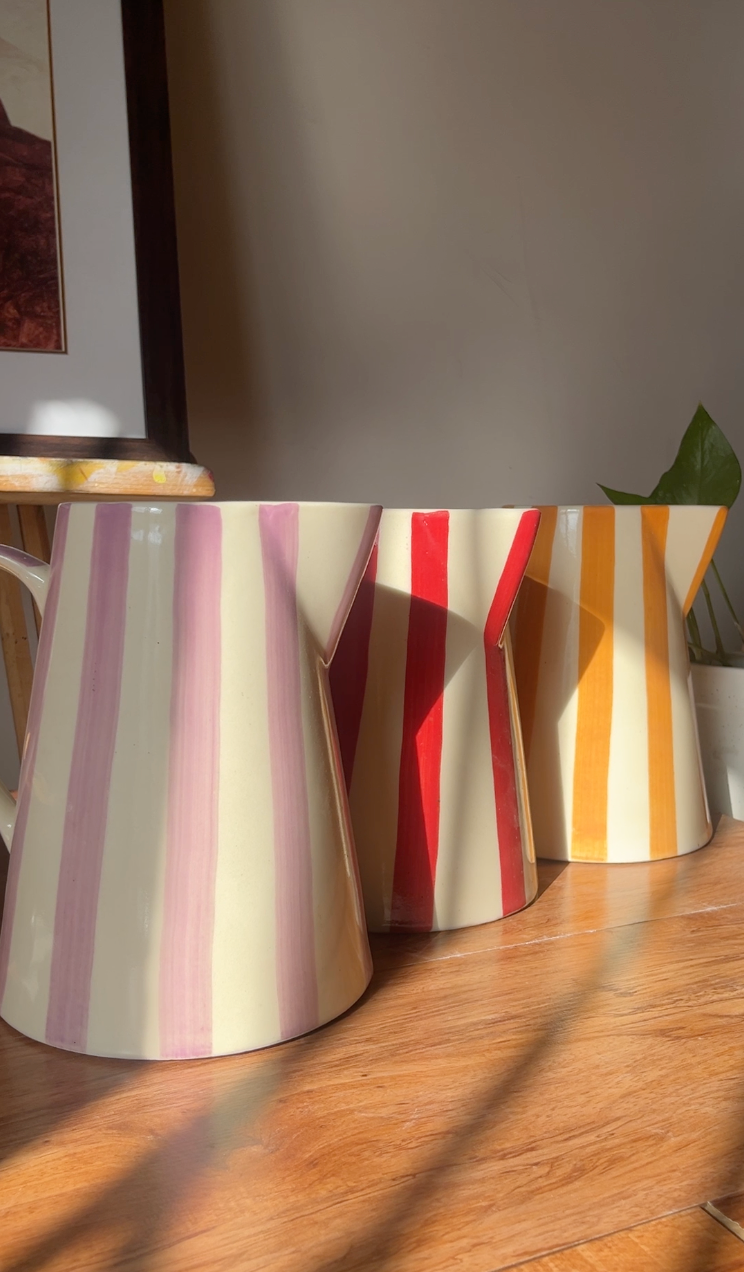 Three colourful ceramic jug vases styled as home decor on a wooden surface