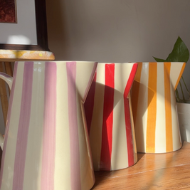Three colourful ceramic jug vases styled as home decor on a wooden surface