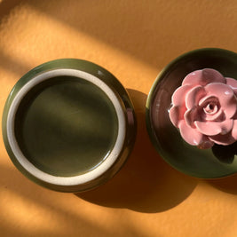 Royal green ceramic incense stick holder with pink flower detail front and back view on a yellow plate. 