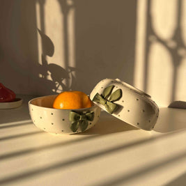 Styled shot of green ceramic bowl with sculptural ribbon bow accent with a fruit