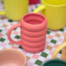Pink matte bubble solid tone mug on a checkered tablecloth with yellow sunbeam and green buttercup in the background