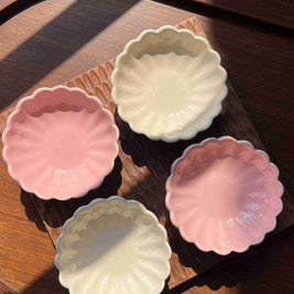 Four small ceramic dishes in pastel colors on a wooden scalloped tray. 