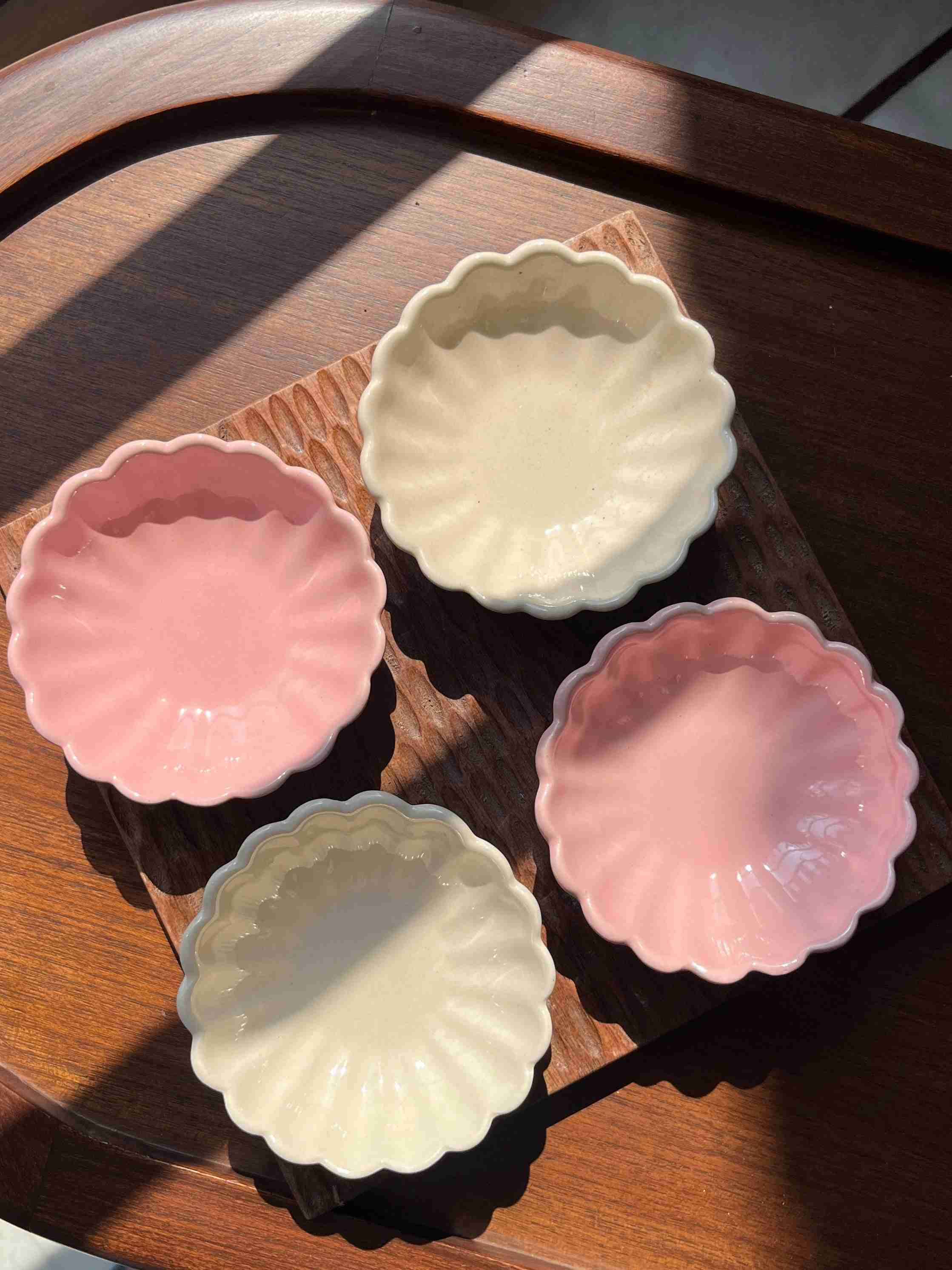 Four small ceramic dishes in pastel colors on a wooden scalloped tray. 