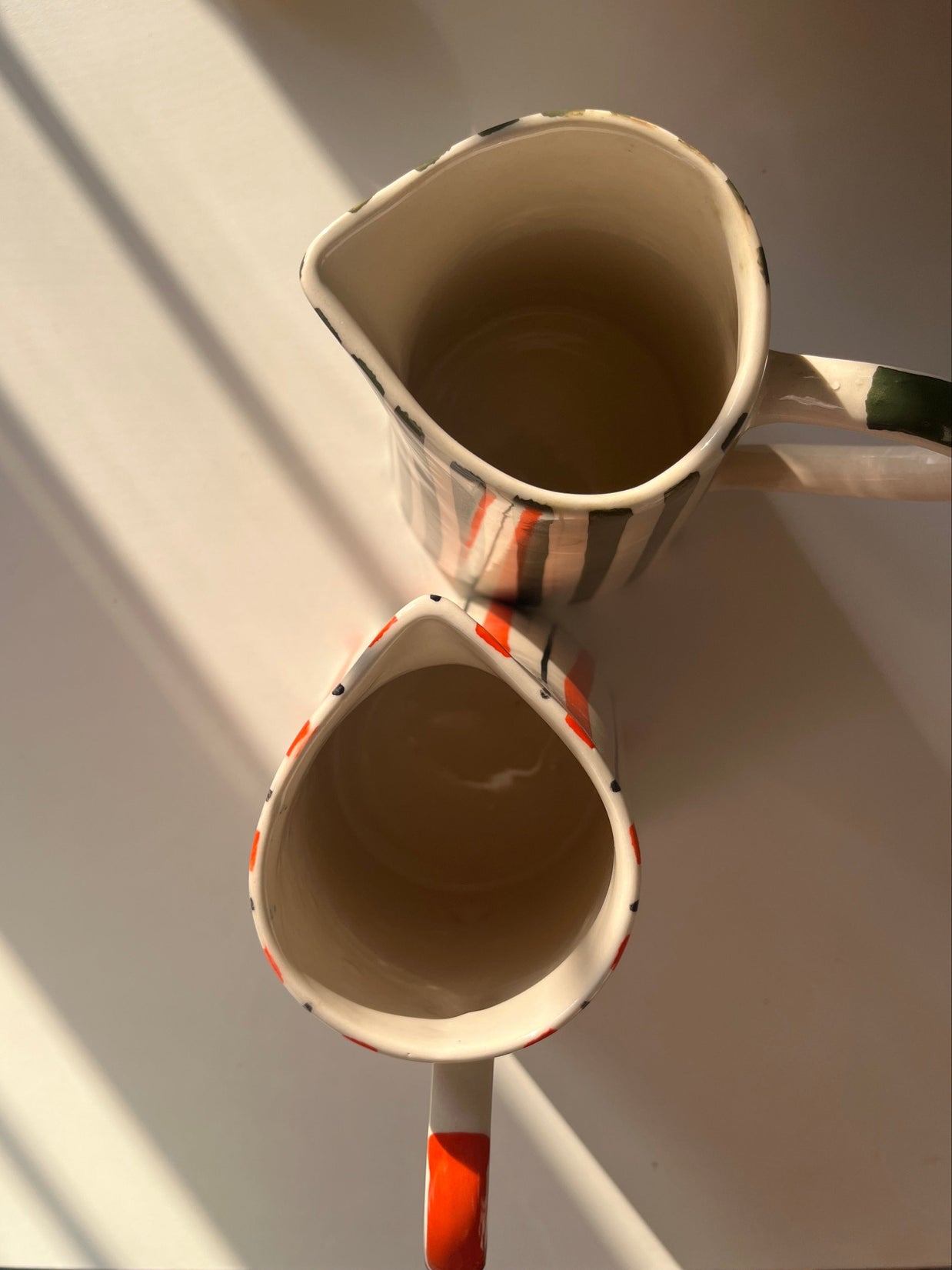 top view of hand-painted ceramic jug with orange stripes and curved handle along with basil jug