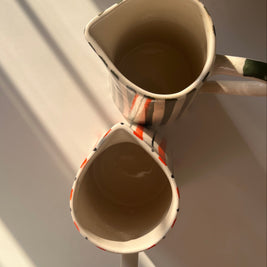 top view of hand-painted ceramic jug with orange stripes and curved handle along with basil jug