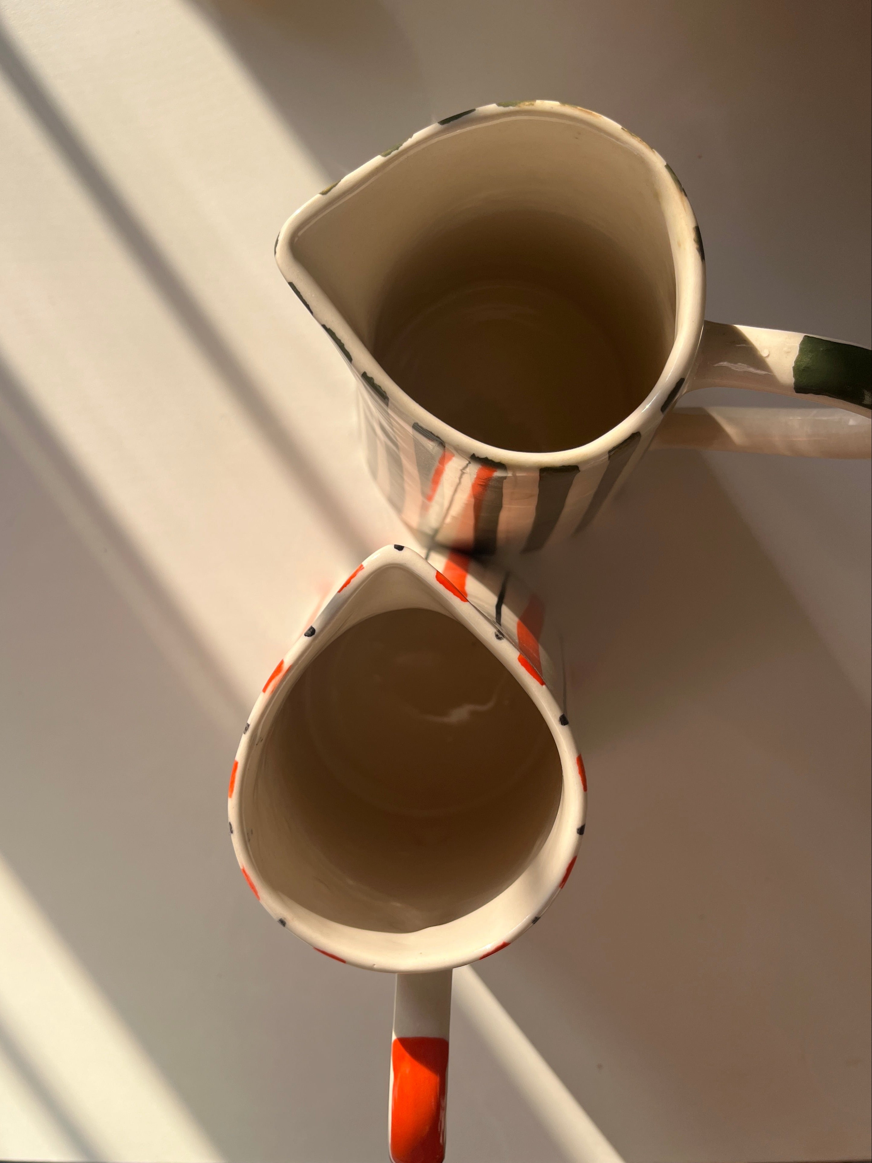 top view of hand-painted ceramic jug with orange stripes and curved handle along with basil jug