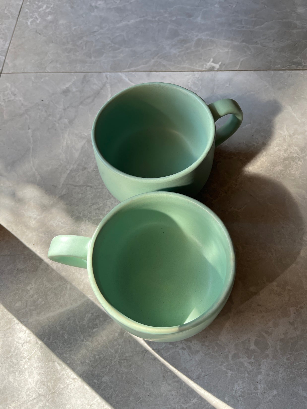 Top-shot of two minimal green ceramic cups with smooth matte texture