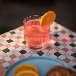 Pink cocktail with an orange slice in a fluted lucid glass on a checkered tablecloth