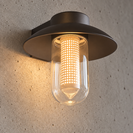 A modern outdoor wall sconce with a dark bronze metal frame and a clear glass cylinder, glowing with a warm yellow light against a textured concrete wall.