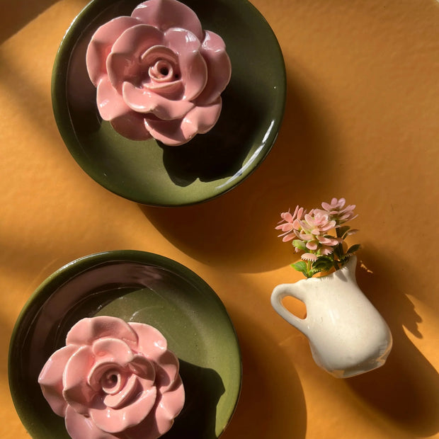 Lifestyle shot of handmade ceramic incense holder with royal green base alongside a small white vase with matching pink flowers, arranged on a large mustard-yellow tray.