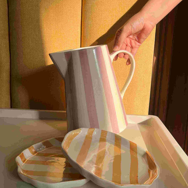 Person holding a striped mug next to matching striped slippers on a yellow background..