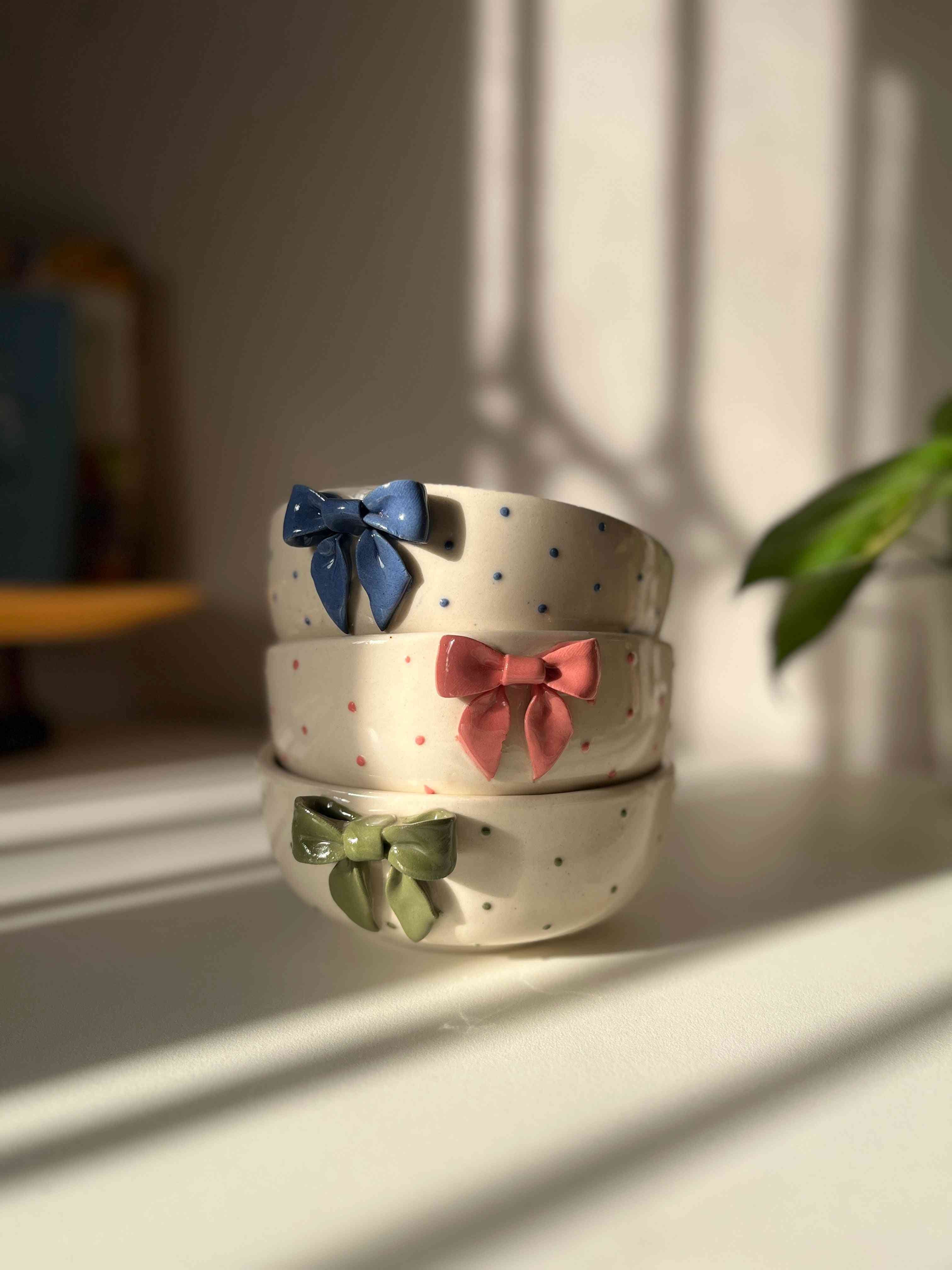 Three ceramic bowls with colorful bow decorations on a light surface.