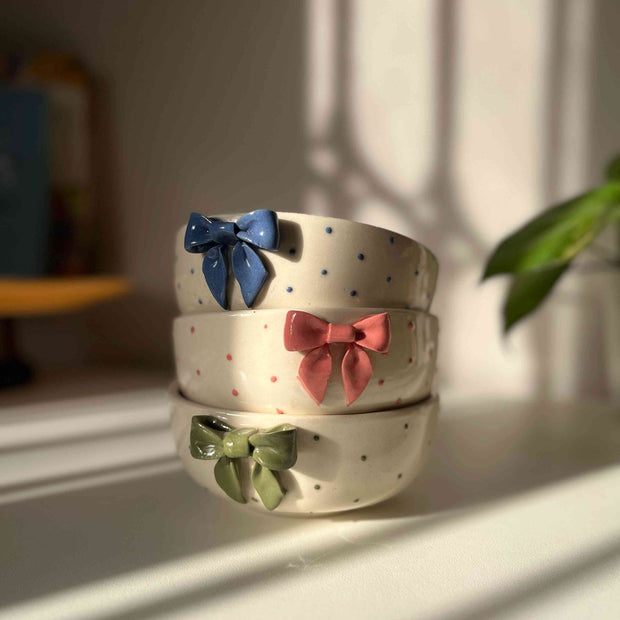 Three ceramic bowls with colorful bow decorations on a light surface.