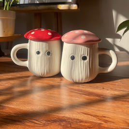 Two mushroom-shaped mugs with colorful caps on a wooden surface.