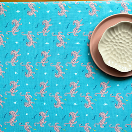 Blue fabric with pink tiger pattern, placed on a wooden surface with a ceramic dishes on top as decor