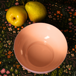 Pink metal bowl on a dark floral-patterned chihiro tablecover with two green pears.