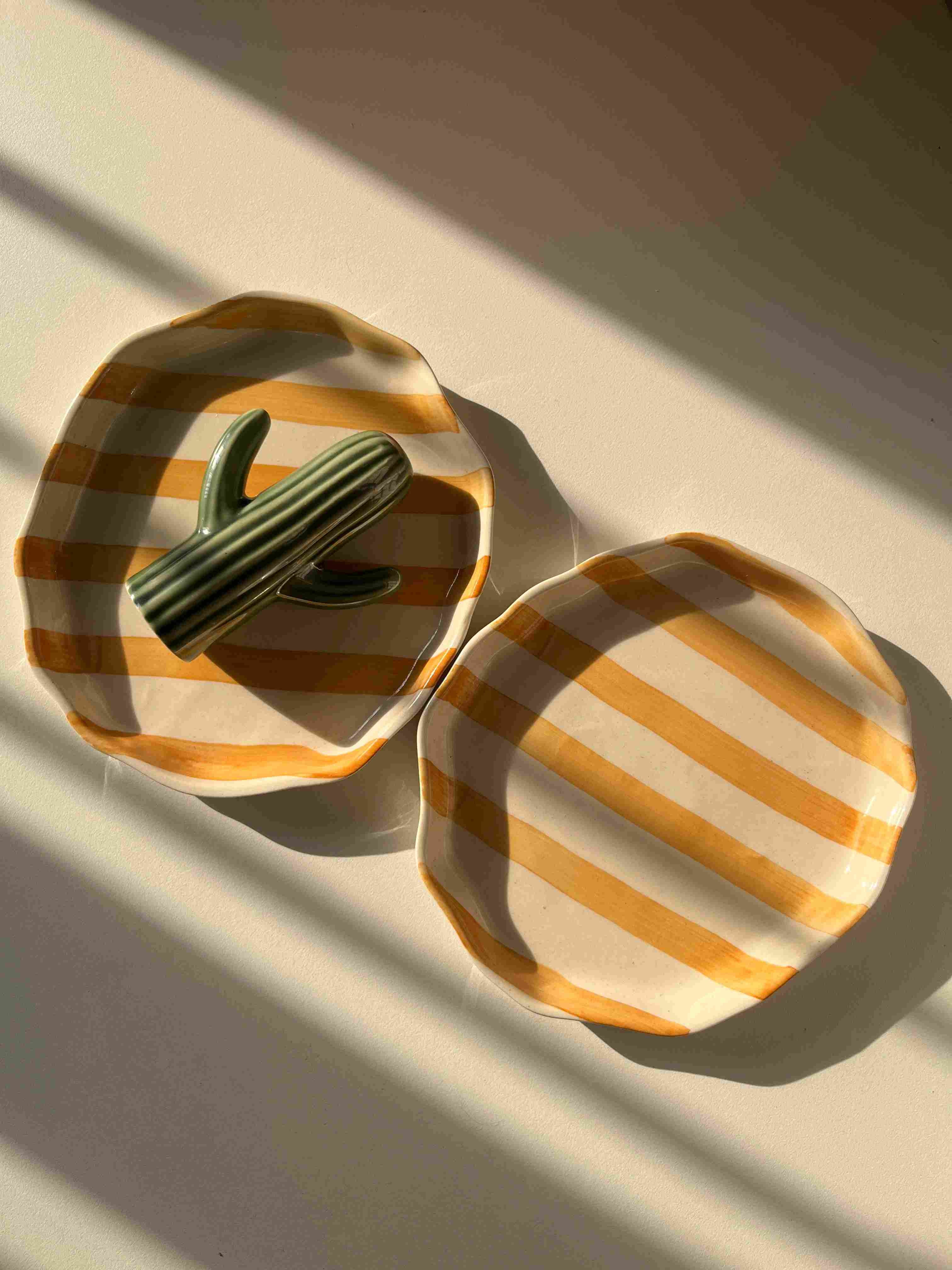 Decorative yellow ceramic tray with striped pattern, freeform shape with cactini in it