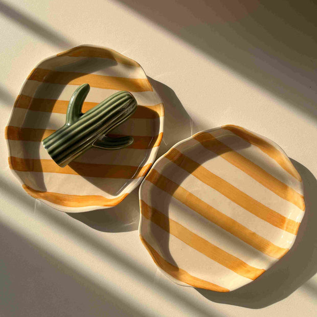 Decorative yellow ceramic tray with striped pattern, freeform shape with cactini in it