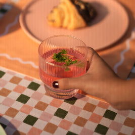 Hand holding a modern fluted glass with a drink on a checkered tablecloth