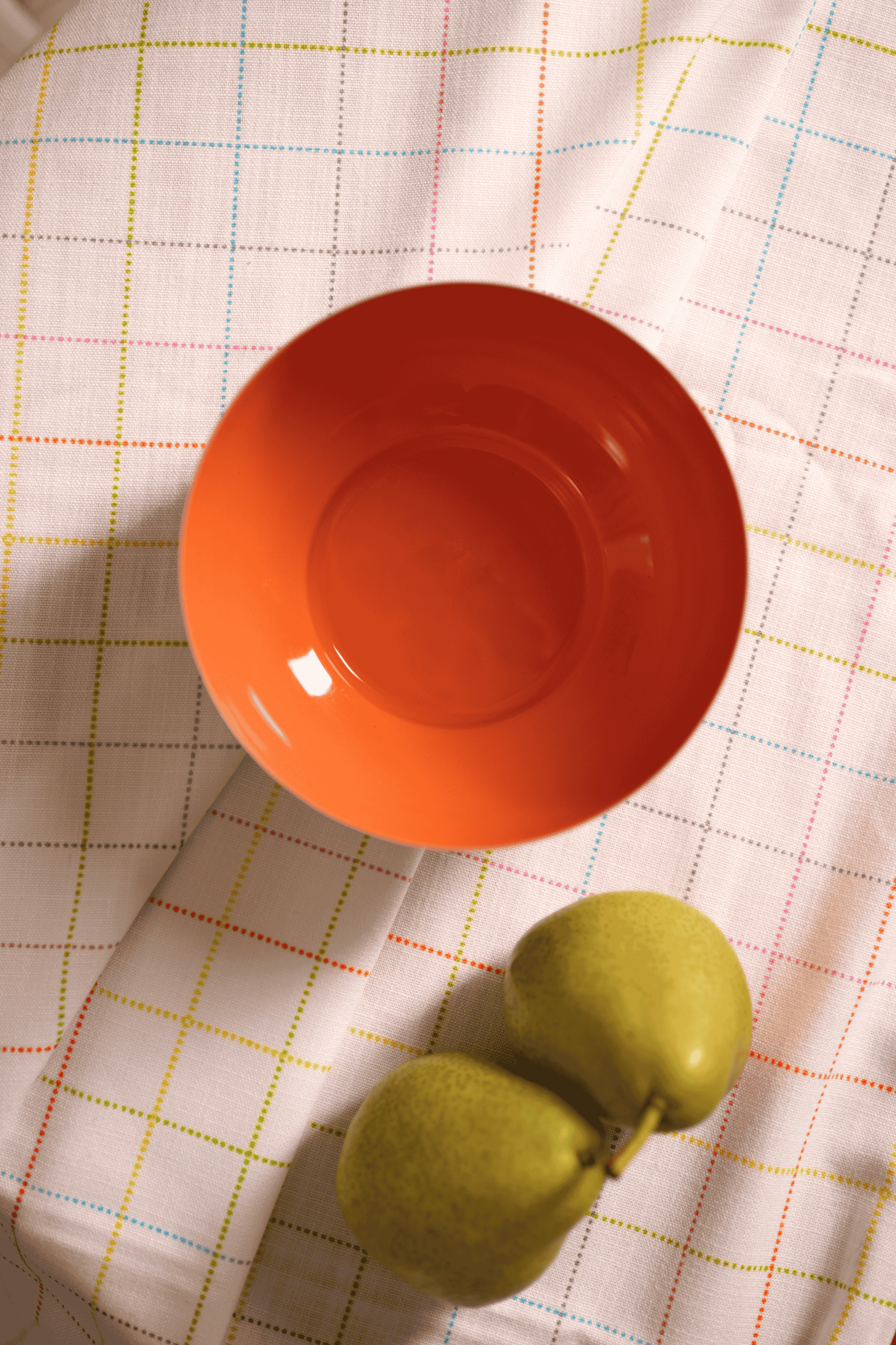 Orange metal bowl and green fruit on a checkered tablecloth