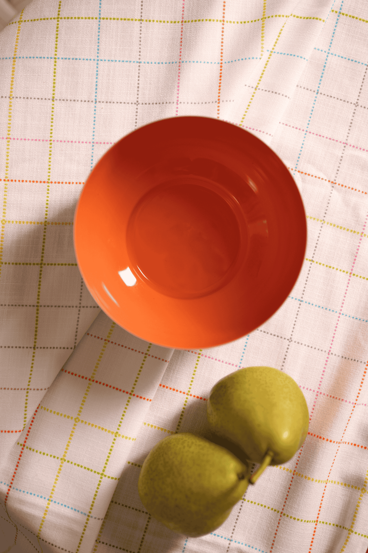 Orange metal bowl and green fruit on a checkered tablecloth