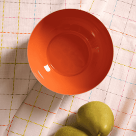 Orange metal bowl and green fruit on a checkered tablecloth