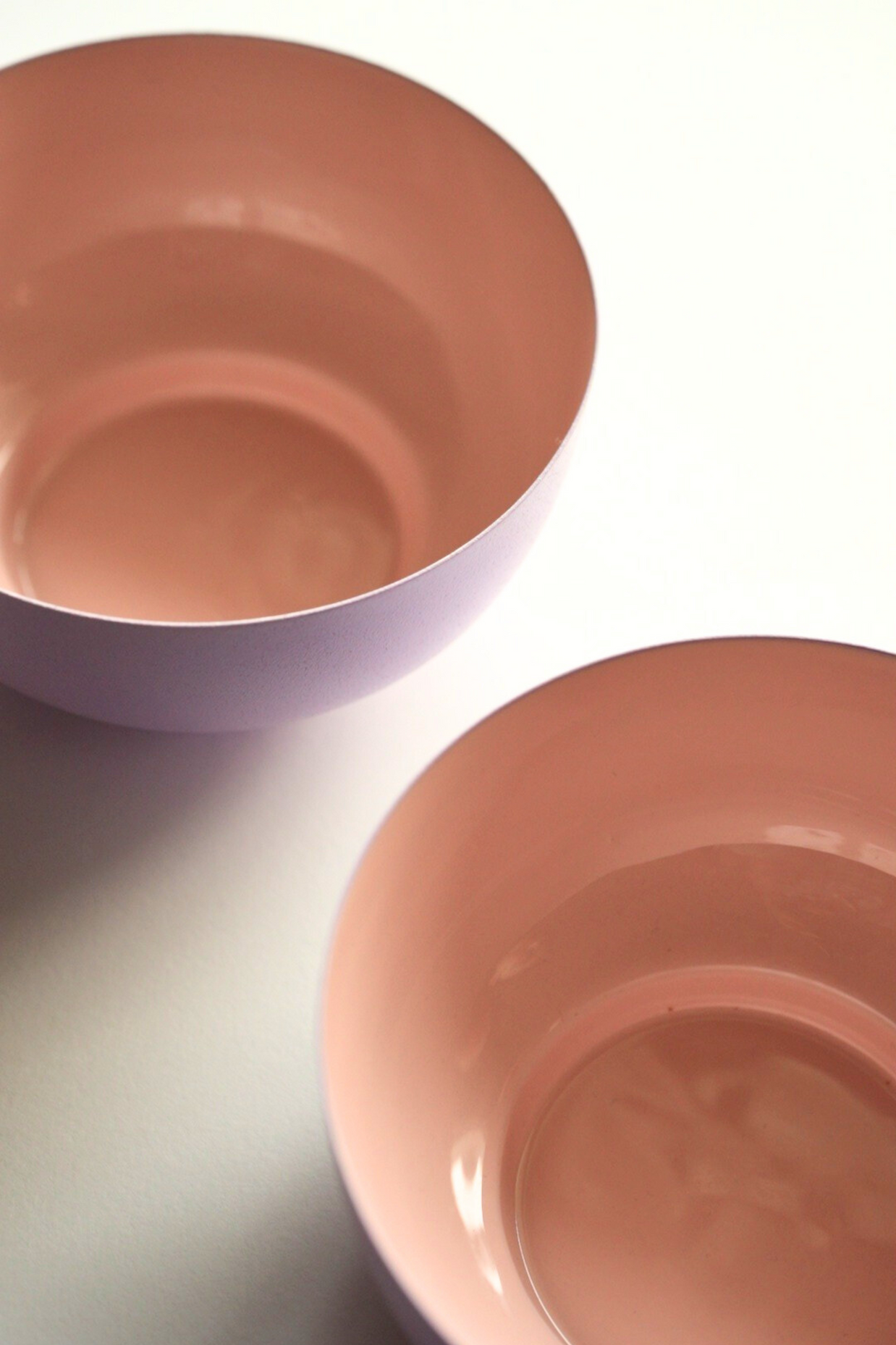 Two pink metal fruit bowls on a light gray surface