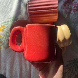 Red ember madam jan ceramic cup with a burnt look held by a hand on a patterned fabric background